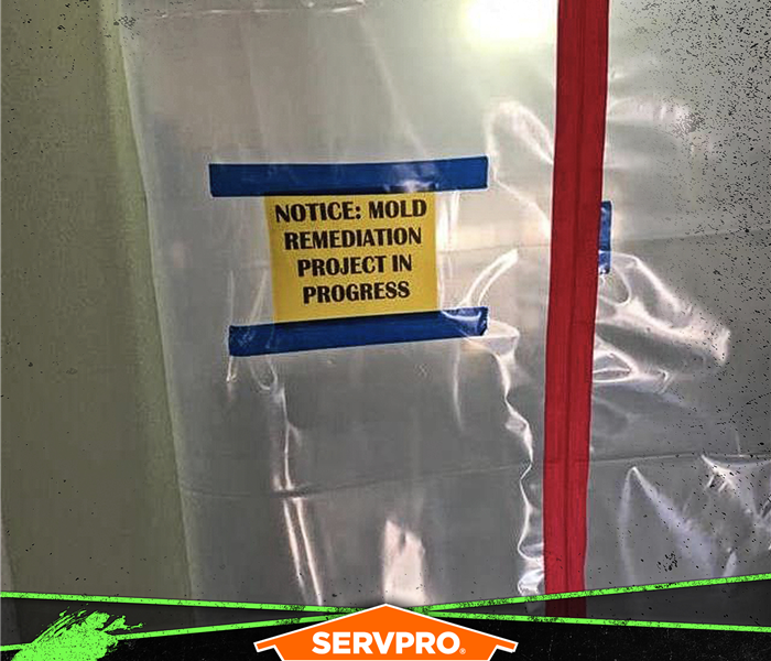 Plastic barrier taped to a wall with a sign saying: NOTICE: MOLD REMEDIATION PROJECT IN PROGRESS